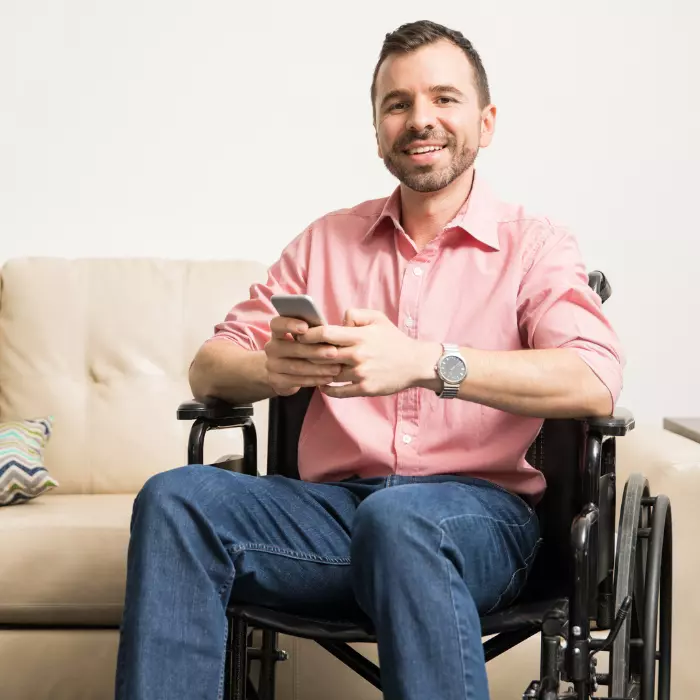 Disabled man sitting in wheelchair in living room smiling at the camera and holding mobile phone