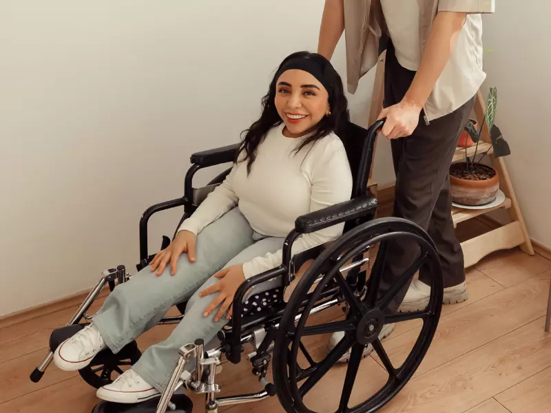 Woman in wheelchair smiling at camera with carer standing behind her