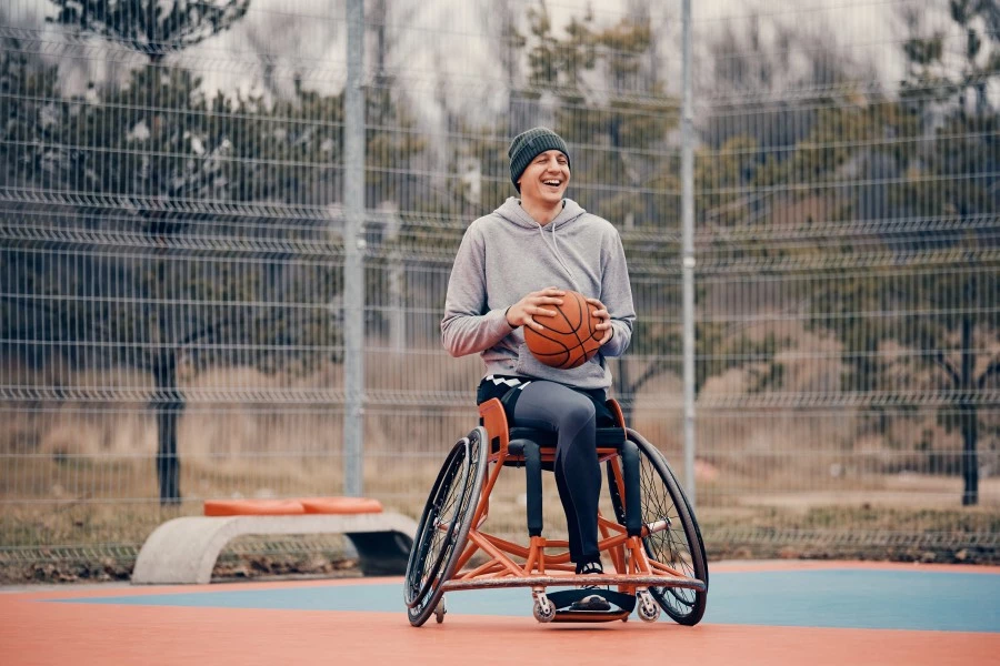 Man in wheelchair holding basketball on court and laughing