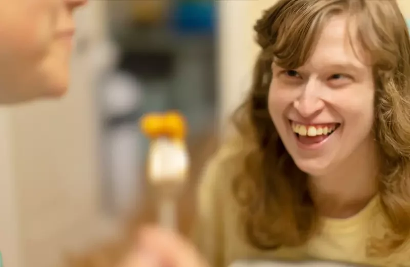 Disabled girl smiling at carer while eating at table