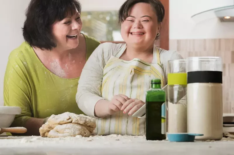Carer with girl with down syndrome baking together in kitchen