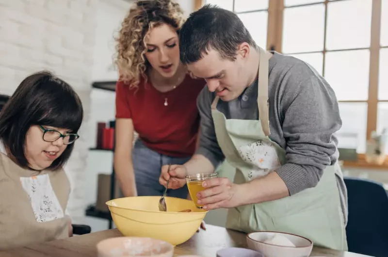 Two friends with down syndrome in cooking class with carer