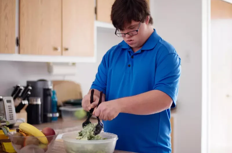 Man with down syndrome making a salad in kitchen